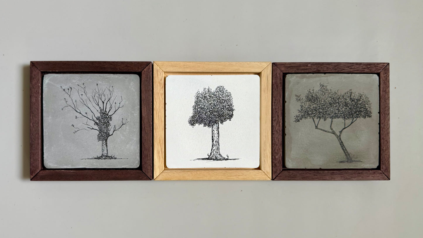 “Set of three framed ink tree drawings by Warren Garland. Each drawn on hand-cast cement tile with varied tree forms and wood frames in warm natural tones.”