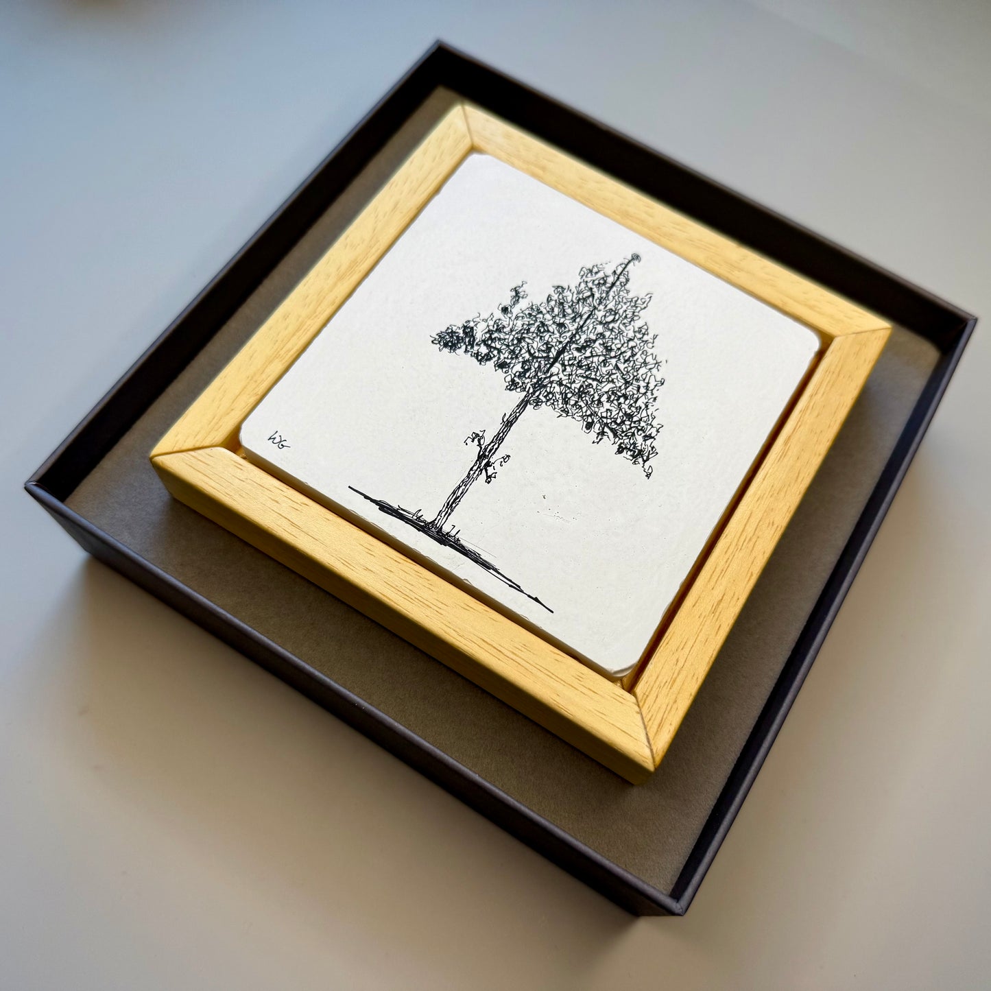 Framed black and white tree drawing on a light surface in a presentation box