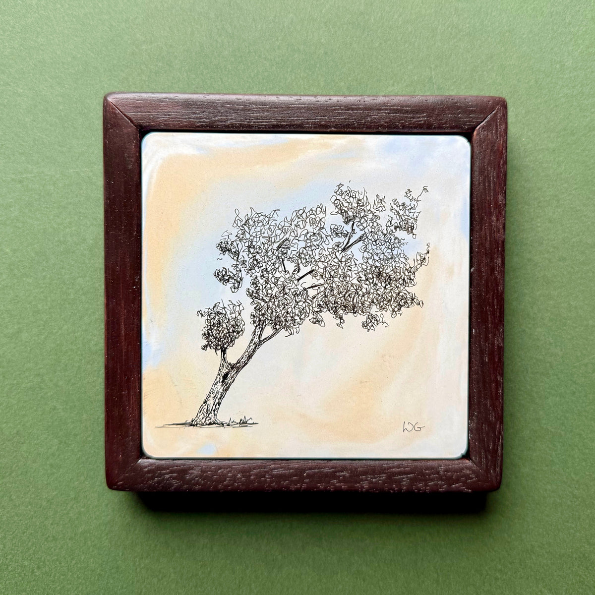 Original black ink drawing of a leaning tree in Cannon Hill Park, Birmingham, on a hand-cast pigmented Portland cement tile. Delicate branches and foliage against a softly coloured surface, presented in a dark wooden frame on a green background.