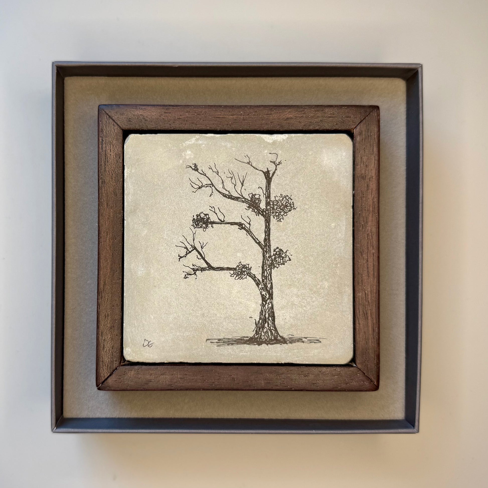 Framed artwork of a tree on cement tile with a wooden frame in a presentation box