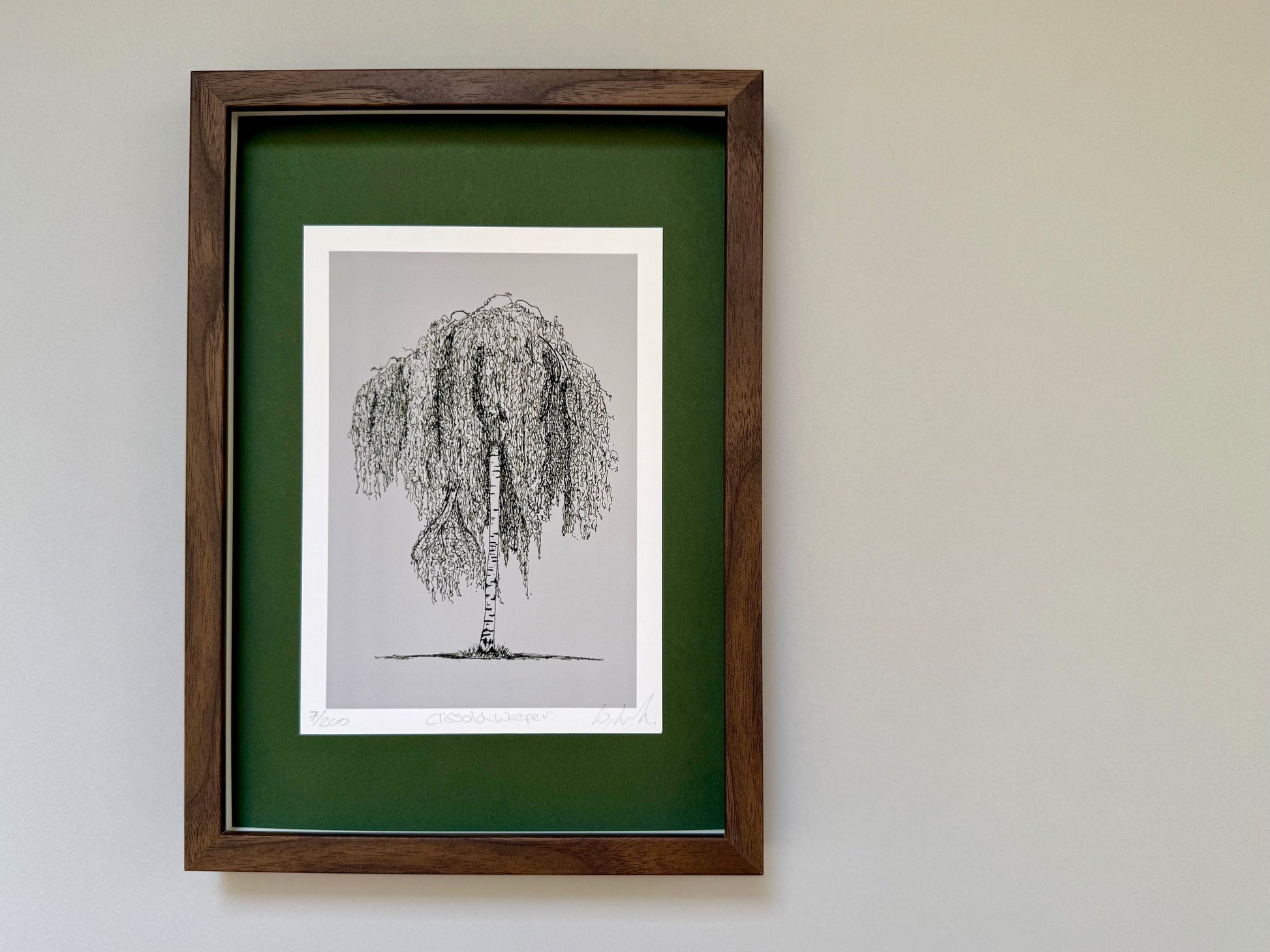 A framed art print featuring a black ink sketch of a weeping tree on a light gray background, surrounded by a white mat and a dark green mat board, all enclosed in a dark brown wooden frame and hung on a light gray wall.