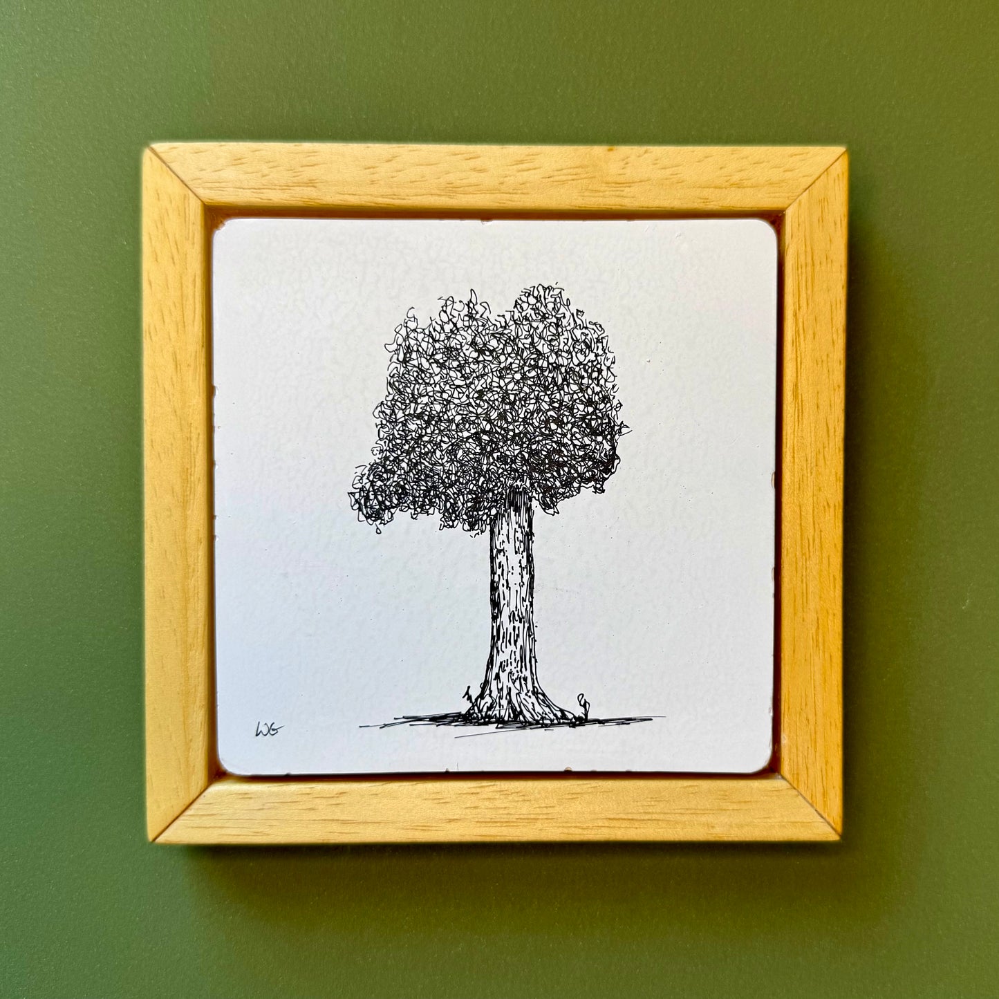 Framed drawing of a tree on a white background with a wooden frame against a green wall.