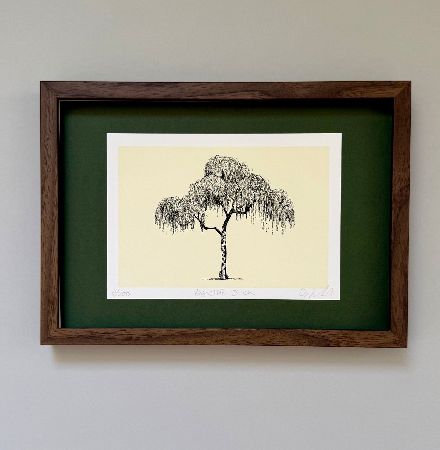 A framed art print featuring a black ink sketch of a weeping tree on a cream background, surrounded by a dark green mat and a dark brown wooden frame, mounted on a light gray wall.