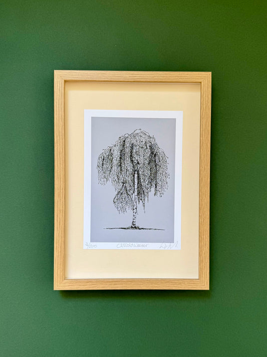 A framed art print featuring a black ink sketch of a weeping tree on a light gray background, matted with a cream border and housed in a light natural wood frame, mounted on a dark green wall.