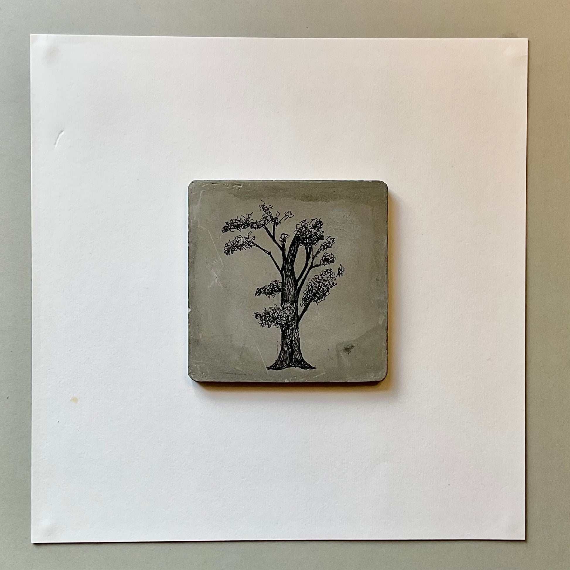 Original ink tree drawing on a square grey cement tile with branching canopy and fine-line detail.

