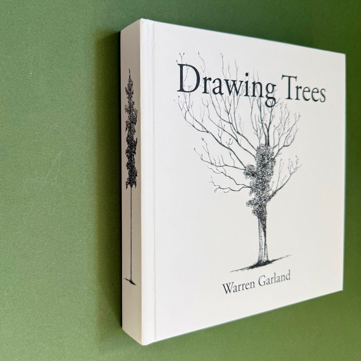 The book 'Drawing Trees' by Warren Garland, featuring a white cover with a black line drawing of a tree, shown standing against a solid green background.