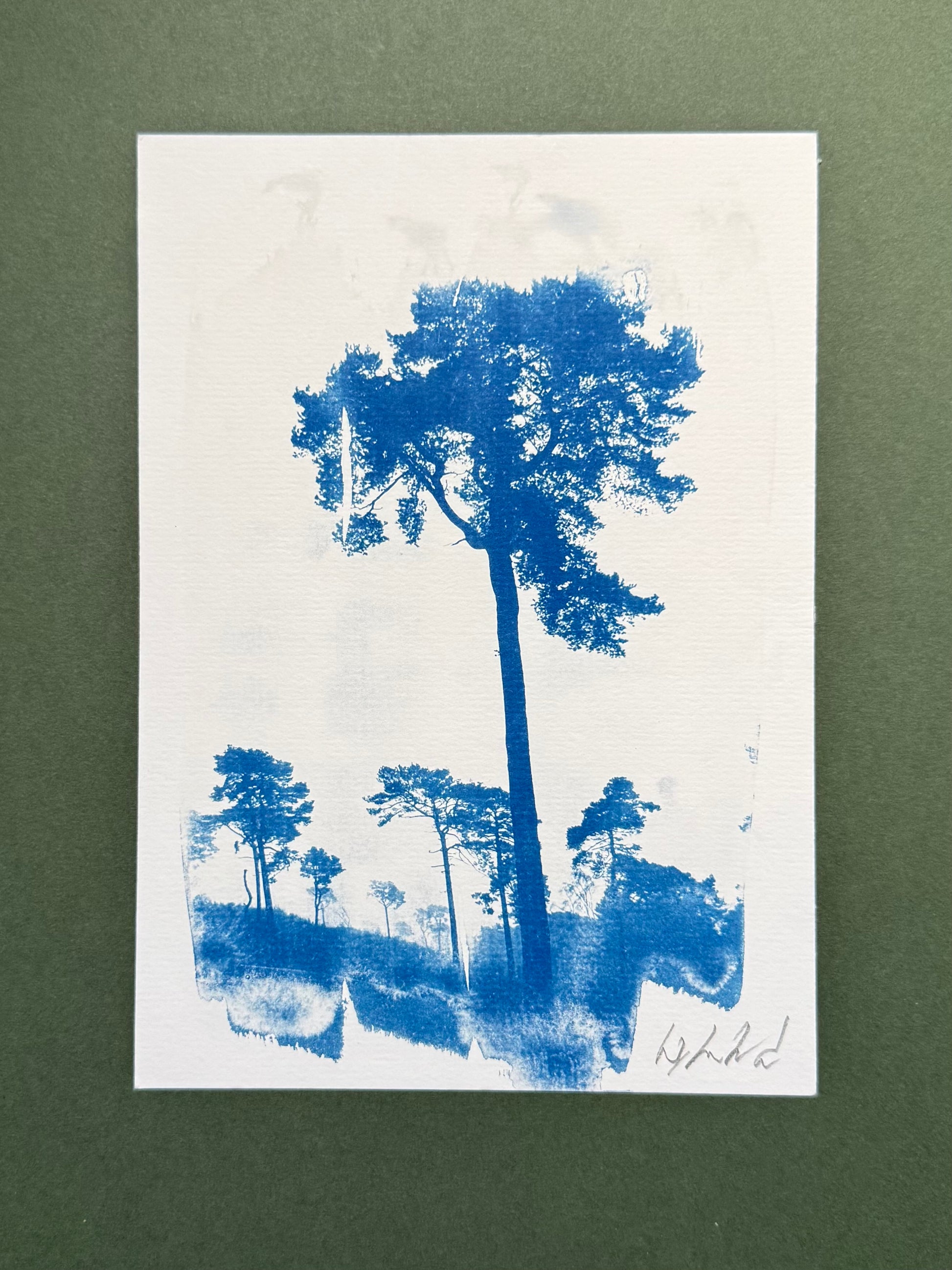 A blue ink tree landscape print on textured white paper, displayed against a dark green background.