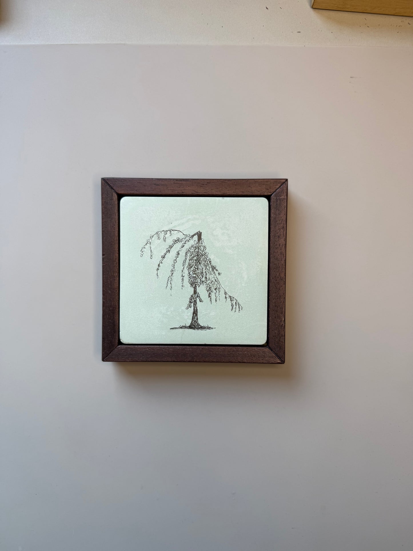 Ink drawing of a weeping willow tree on a hand-cast cement tile, set in a dark wood frame against a pale grey wall.