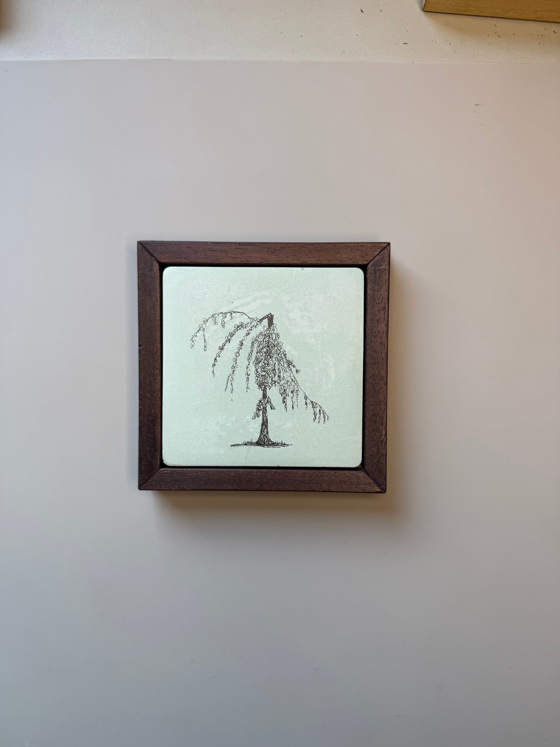 Ink drawing of a weeping willow tree on a hand-cast cement tile, set in a dark wood frame against a pale grey wall.