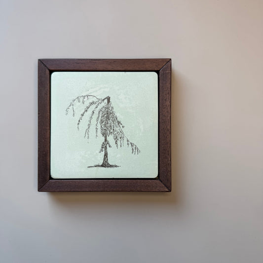 Ink drawing of a weeping willow tree on a hand-cast cement tile, set in a dark wood frame against a pale grey wall.