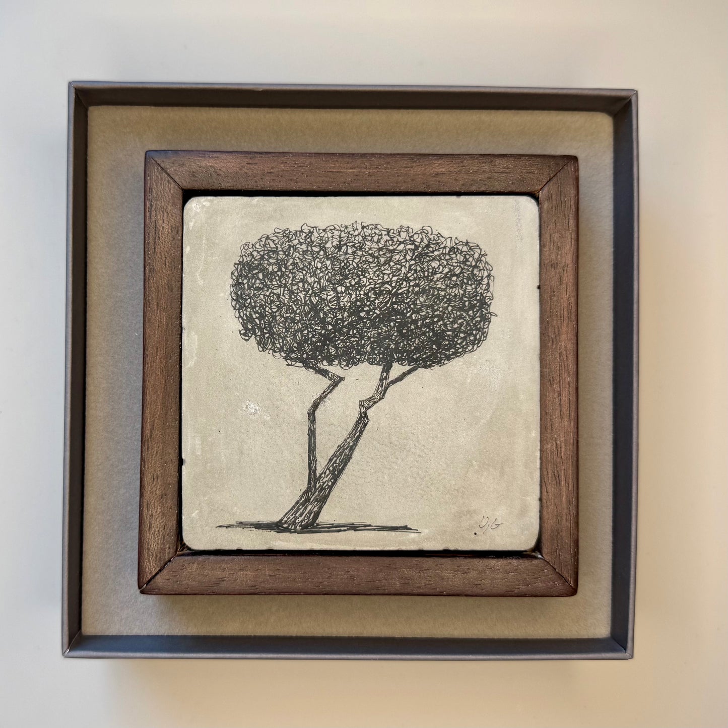 Framed artwork of a tree on a cement tile in a presentation box