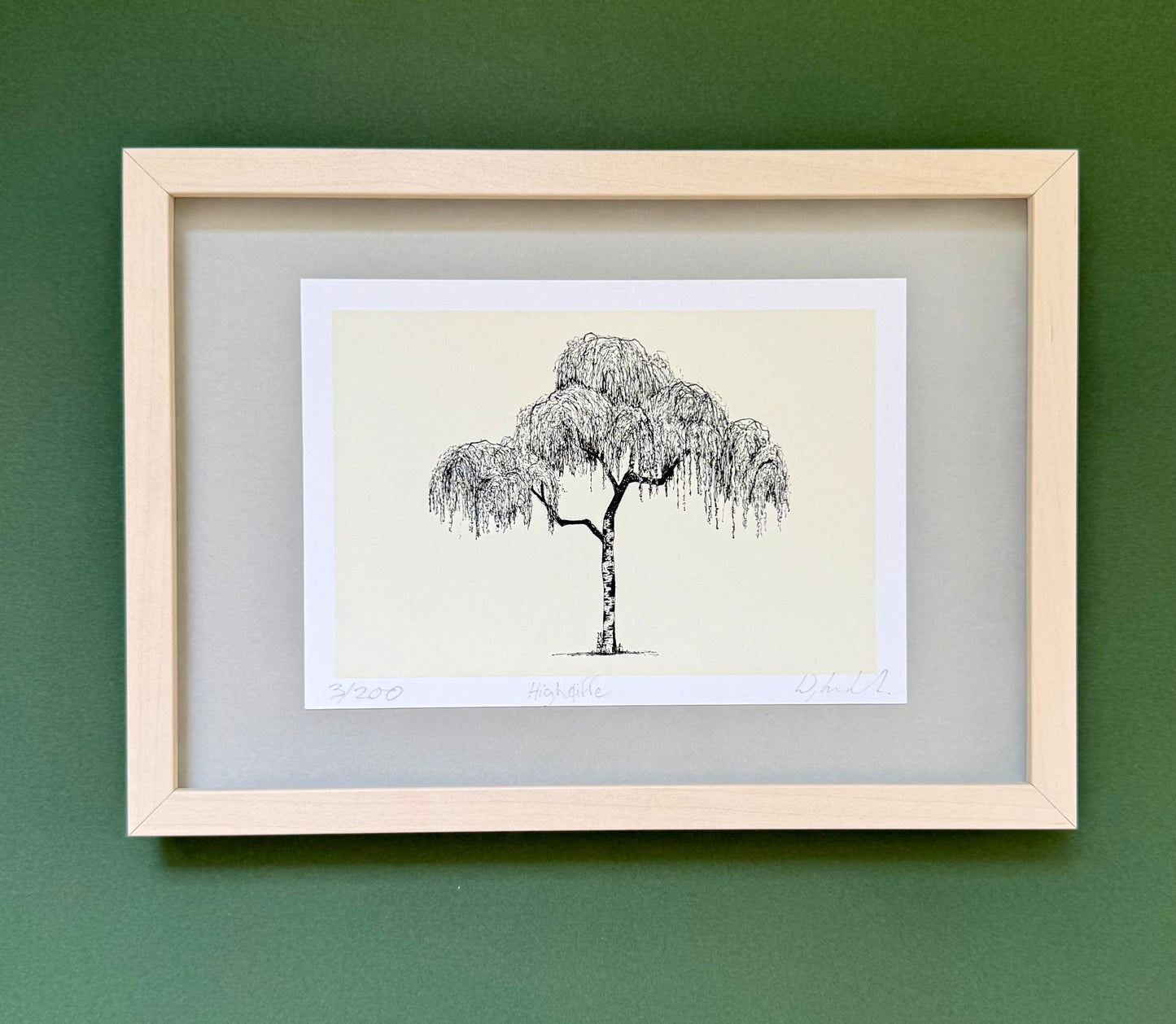 A framed art print featuring a black ink sketch of a weeping tree on a cream background, set in a light wood frame against a dark green wall.