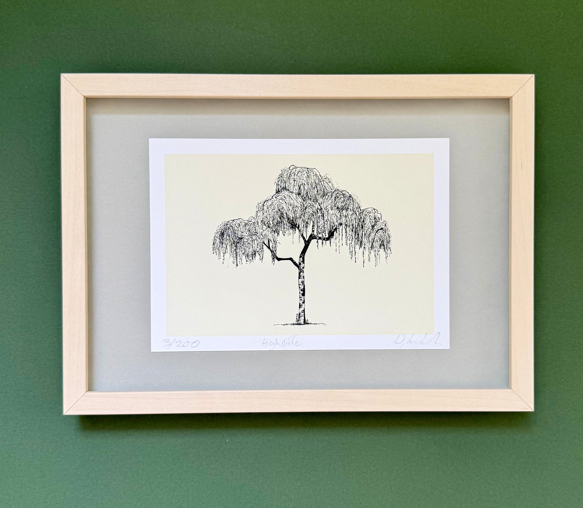 A framed art print featuring a black ink sketch of a weeping tree on a cream background, set in a light wood frame against a dark green wall.